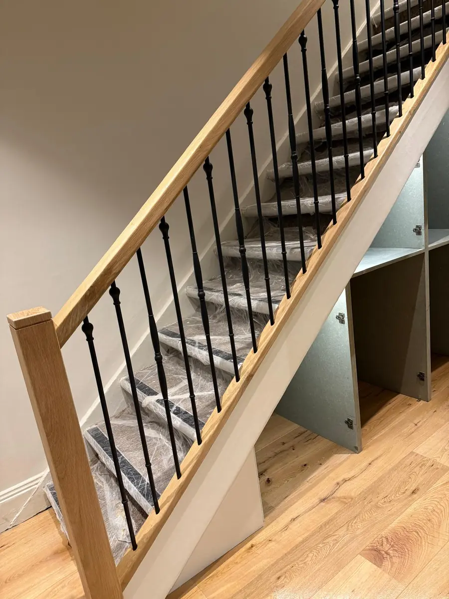 Side view of an oak handrail and black iron spindles on a staircase